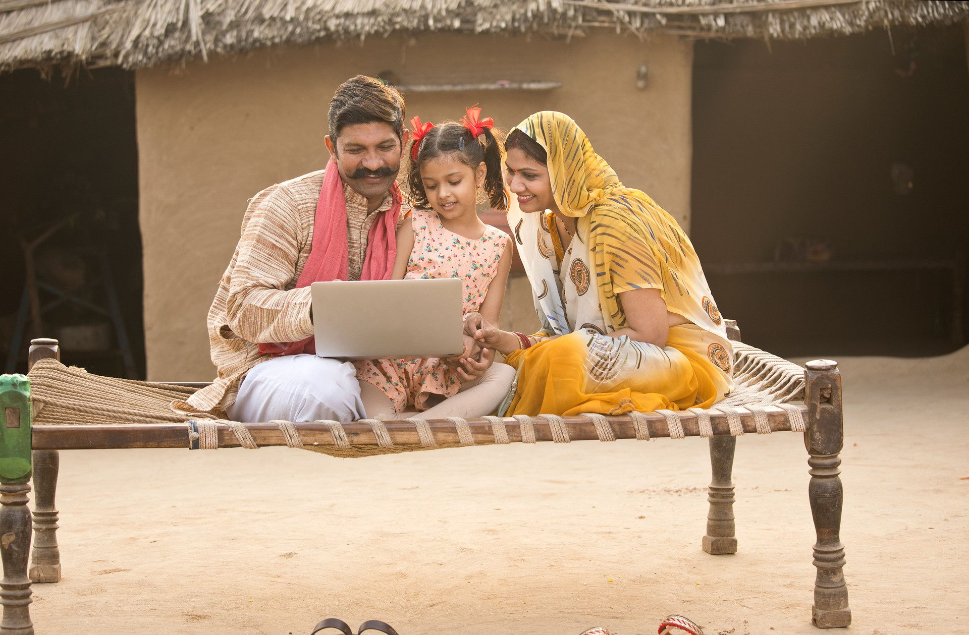 Rural Indian family using laptop on traditional bed at village